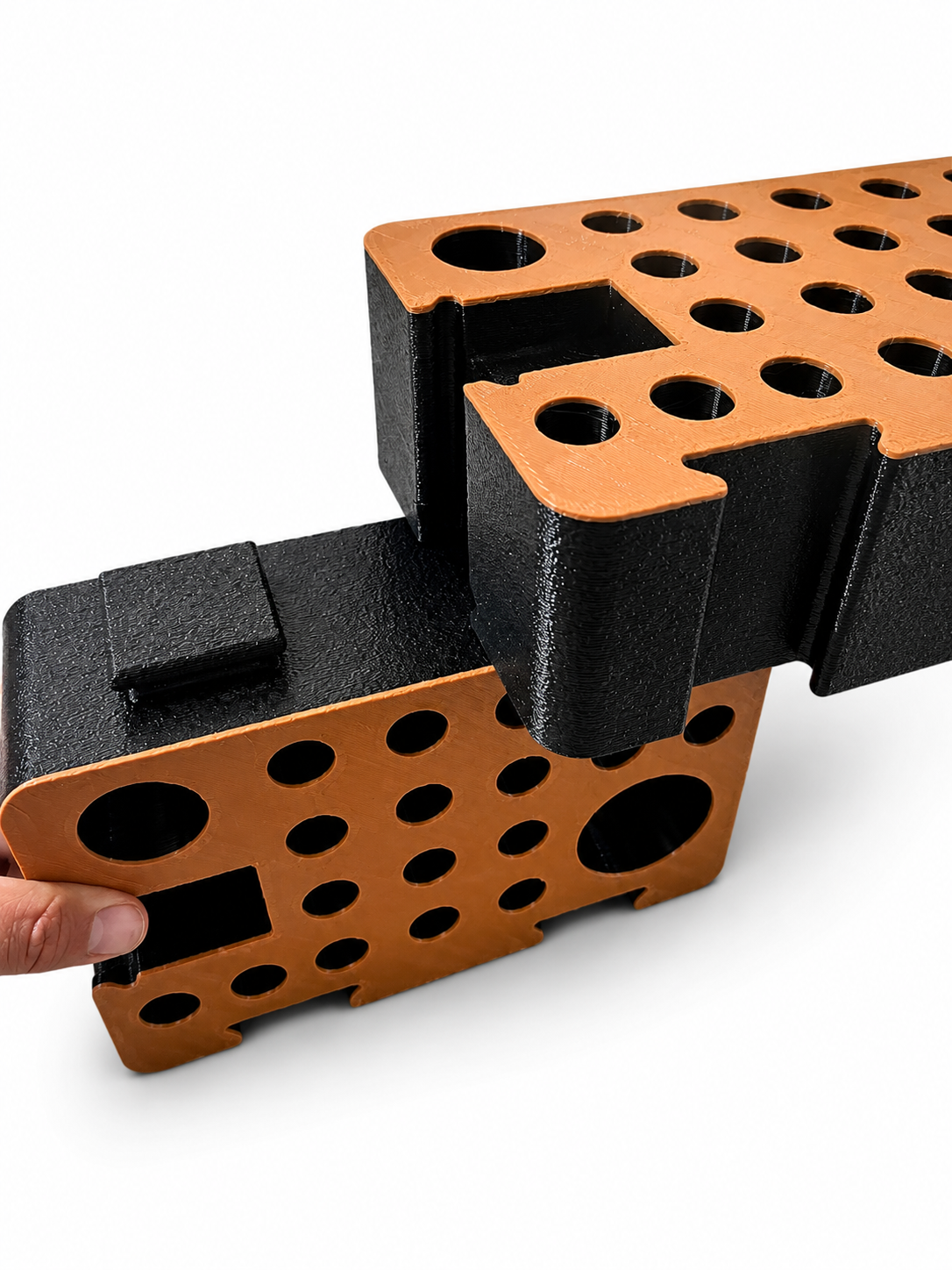 A hand sliding one orange and black D-Block into another, demonstrating how the blocks interlock